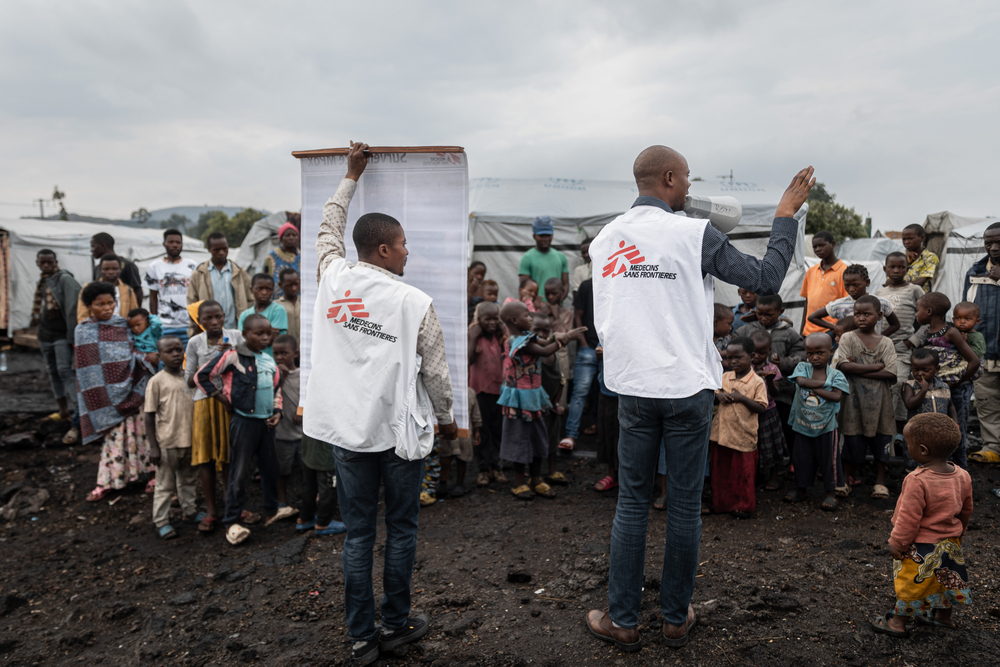 MSF Health Promoters use posters and a megaphone to spread information about mpox prevention strategies in the Buhimba displacement Camp, on the outskirts of Goma