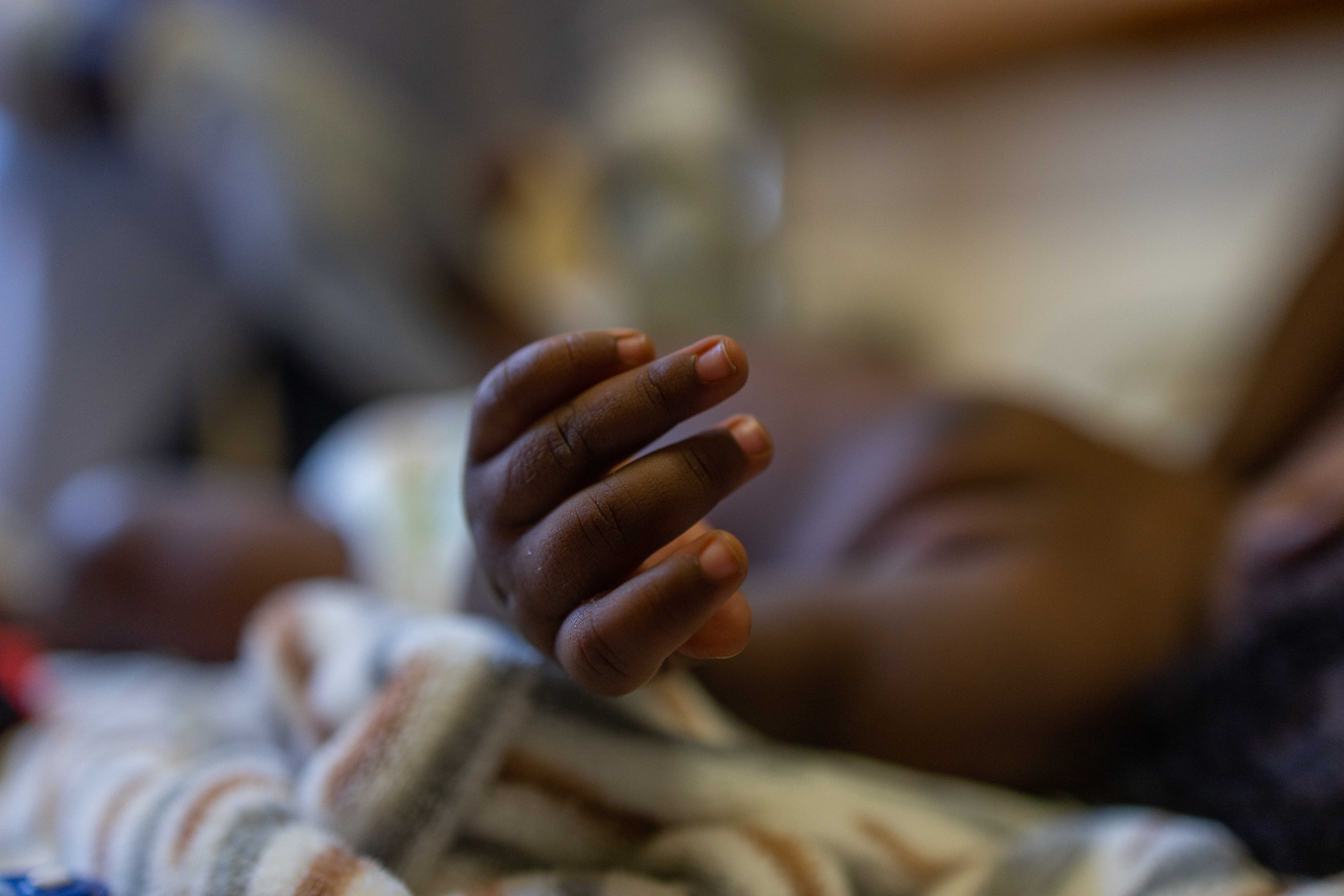 The small hand of a sick child lying on a bed is in focus.