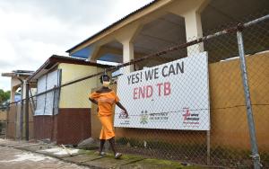 Woman walking past clinic with yes we can end TB sign
