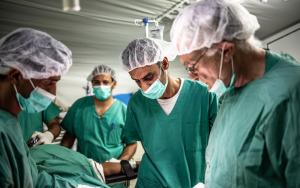 four surgeons in green scrubs perform a trauma surgery.