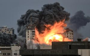 Image showing people standing on a rooftop watch as a ball of fire and smoke rises above a building in Gaza City on October 7, 2023 during an Israeli air strike that hit the Palestine Tower building.