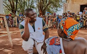 A doctor administers a meningitis vaccination to a woman. In the background is a long queue of people waiting for their turn to be vaccinated.