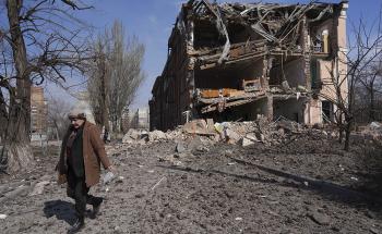 A woman walks past building damaged by shelling in Mariupol, Ukraine, Sunday, March 13, 2022. The surrounded southern city of Mariupol, where the war has produced some of the greatest human suffering, remained cut off despite earlier talks on creating aid or evacuation convoys. 