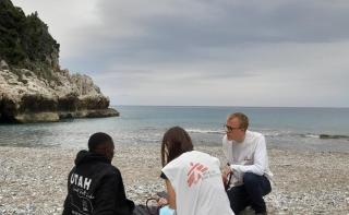A man is sitting on a beach, catching his breath, while an MSF doctor is examining him and chatting about his mental health.