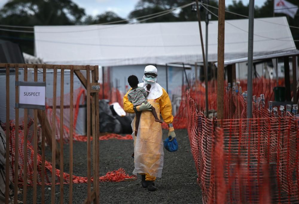A health worker in protective clothing carries a child suspected of having Ebola in the MSF treatment center
