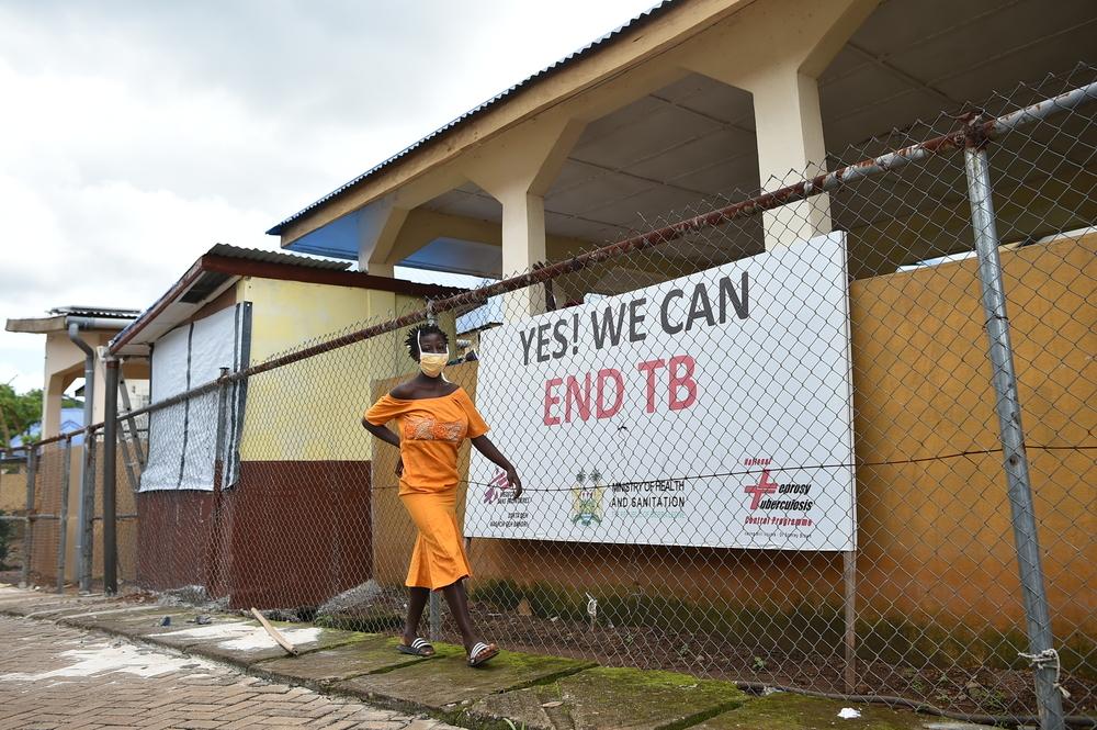 Woman walking past clinic with yes we can end TB sign