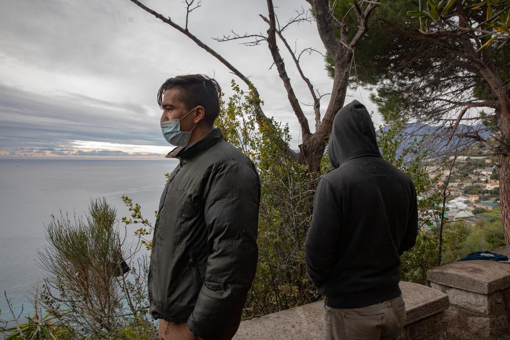 Two refugees look out over the Mediterranean Sea above Ventimiglia, Italy. December 2020.