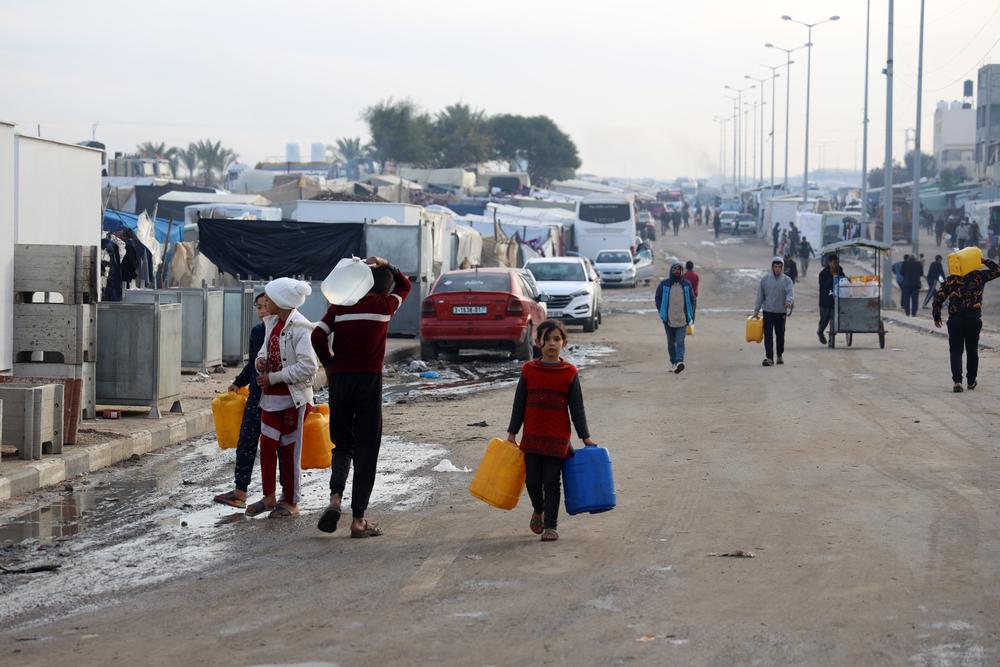 Palestinian men and children are carry water bottles in Tal Al-Sultan, a neighborhood in the southern Gaza town of Rafah.