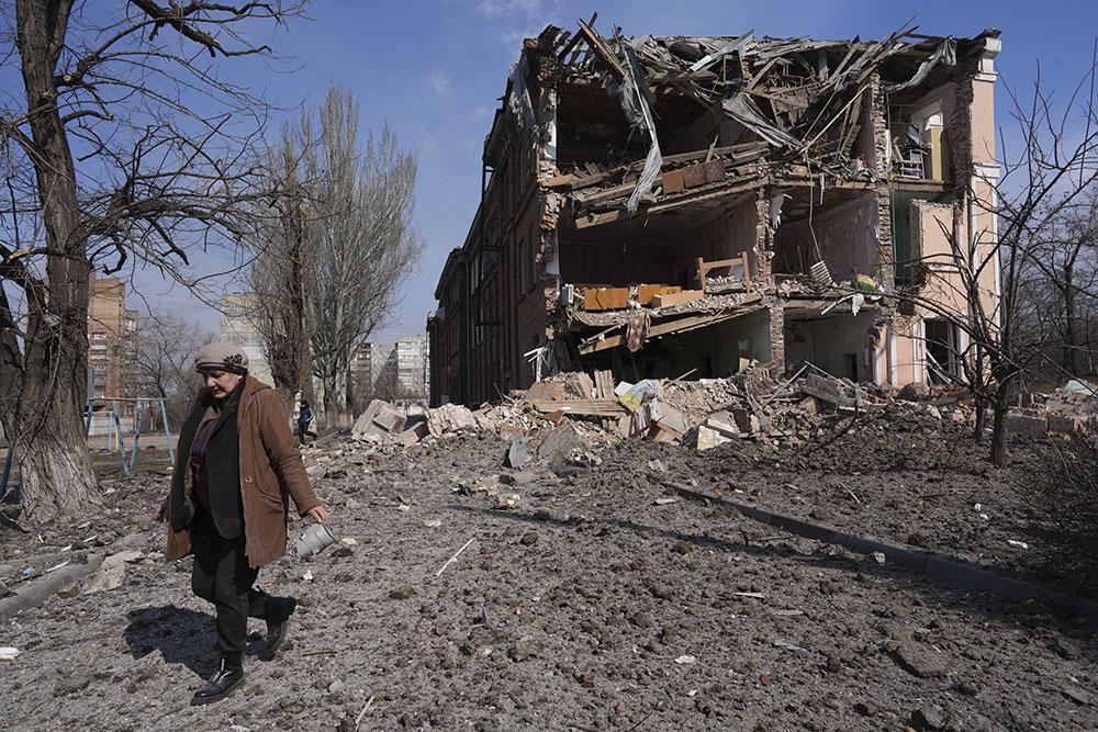 A woman walks past building damaged by shelling in Mariupol, Ukraine, Sunday, March 13, 2022. The surrounded southern city of Mariupol, where the war has produced some of the greatest human suffering, remained cut off despite earlier talks on creating aid or evacuation convoys.