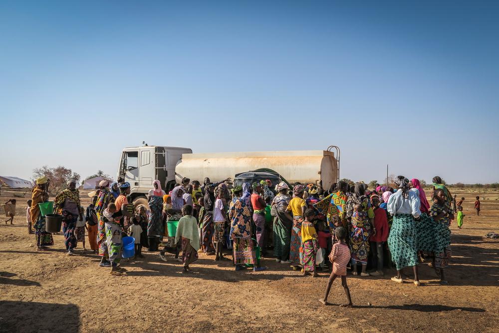 Displaced people standing next to tanker trucks where it is distributed in the camp
