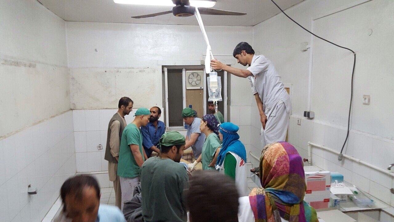 surgery and trauma teams work on a patient while an assistant holds the IV bags above their heads