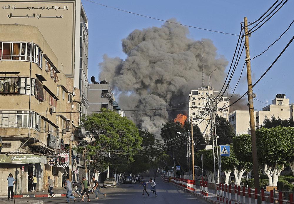 People run away from the vicinity of Al-Sharouk tower as it collapses after being hit by an Israeli air strike, in Gaza City, on May 12, 2021. 