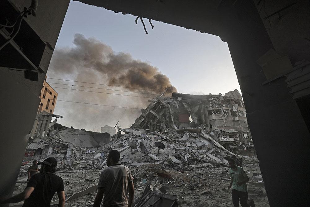  People gather amidst the rubble in front of Al-Sharouk tower that collapses after being hit by an Israeli air strike, in Gaza City, on May 12, 2021.