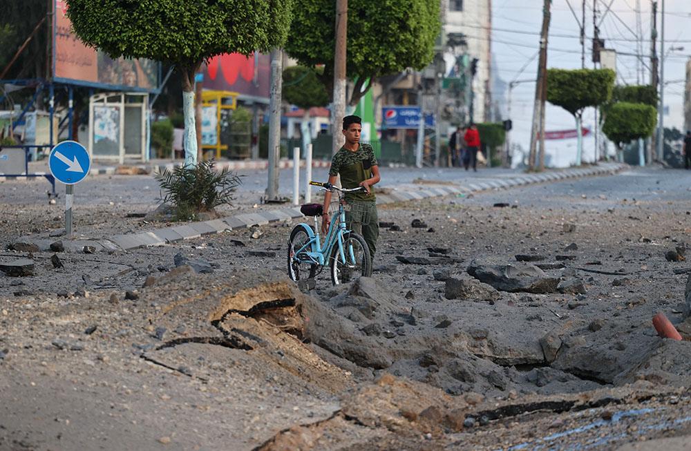 A Palestinian man pushes his bicycle past a crater on the ground near the al-Sharouk tower, which housed the bureau of the Al-Aqsa television channel in the Gaza Strip, after it was destroyed by an Israeli air strike, in Gaza City, on May 13, 2021. 