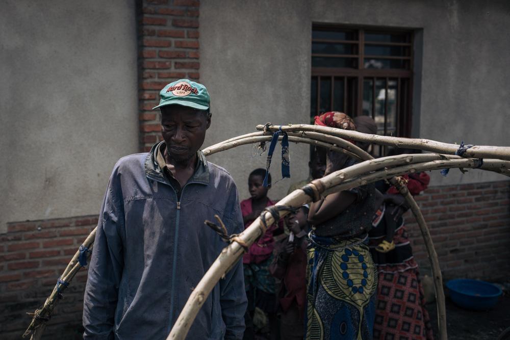 Ponsie, a 54-year-old displaced man, stands in the middle of a branch shelter he is building to protect his children from sleeping outside