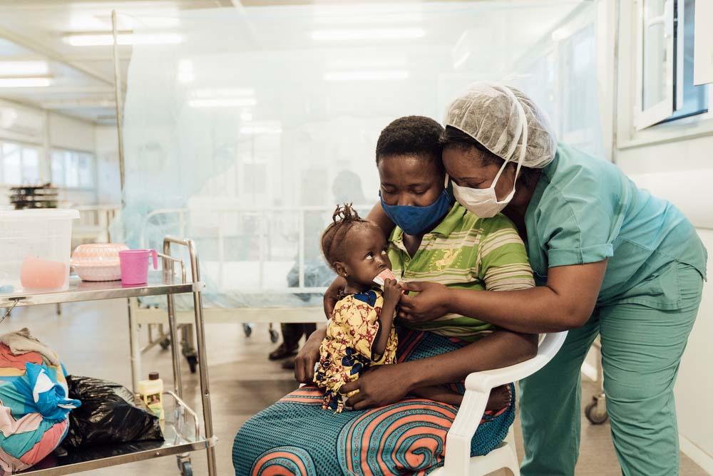 A picture of an MSF Staff member feeding a child with her mother.