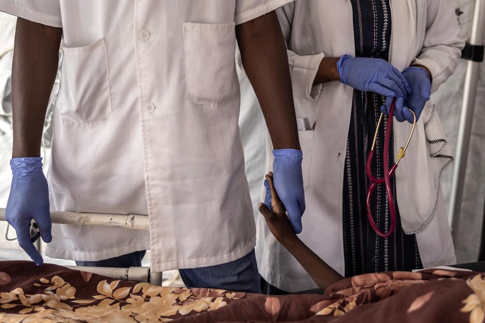 A doctor and nurse standing beside patient's bedside, one holding patient's hand, palliative care
