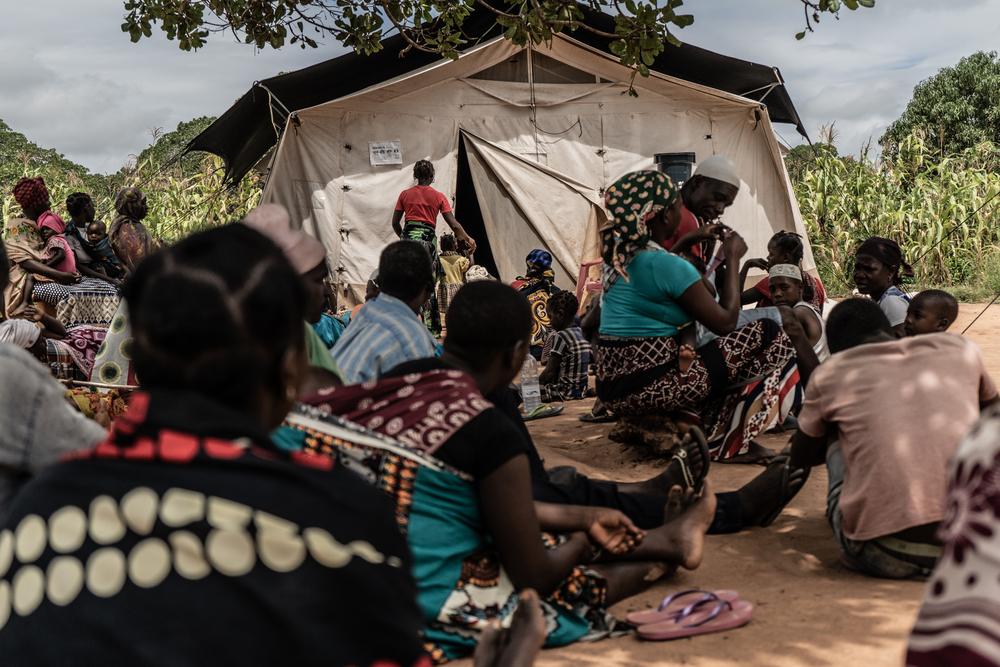 Patients wait in a clearing under a tree to be seen by a medical team