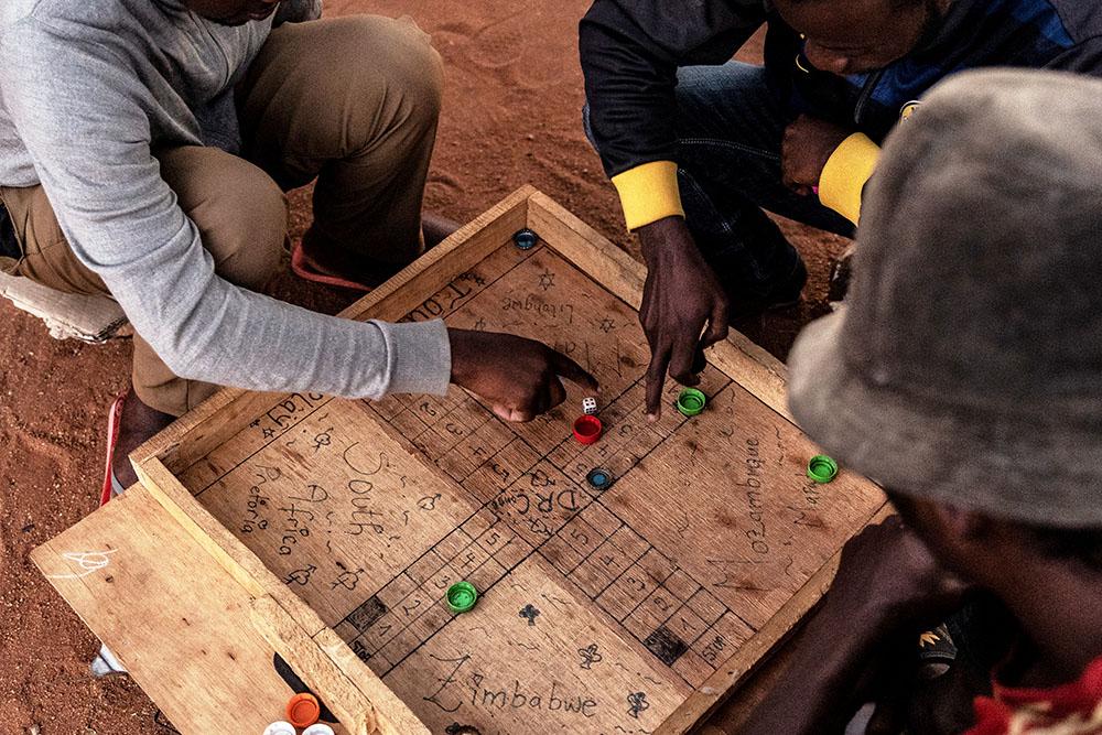 Men staying at a shelter for refugees in Musina, South Africa play a game of "Ludo" on a board with the names of the various countries some of the migrants who have stayed at the camp come from.
