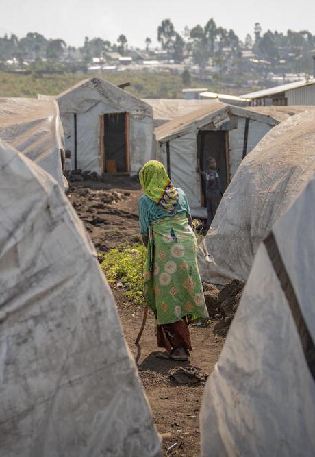 A woman makes her way through a village of white tents. In these displacement camps, sexual and gender-based violence is rife.