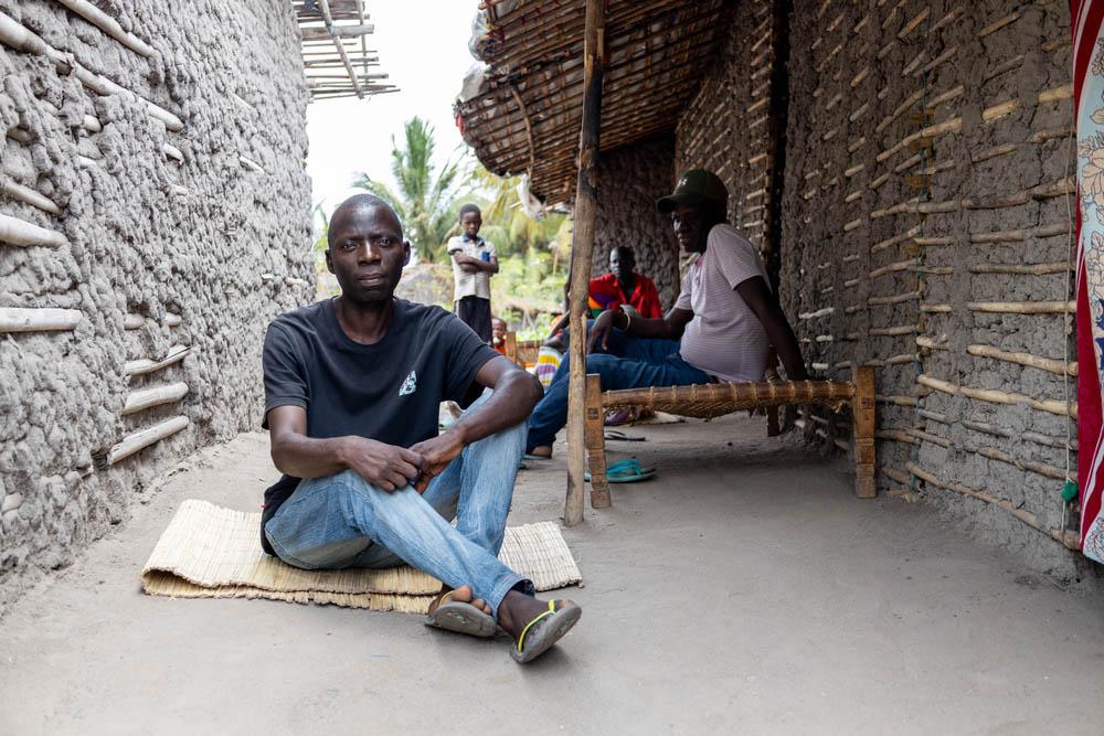 A man site on a mat beween two buildings. War and conflict has a devastating effect on those living with chronic diseases.
