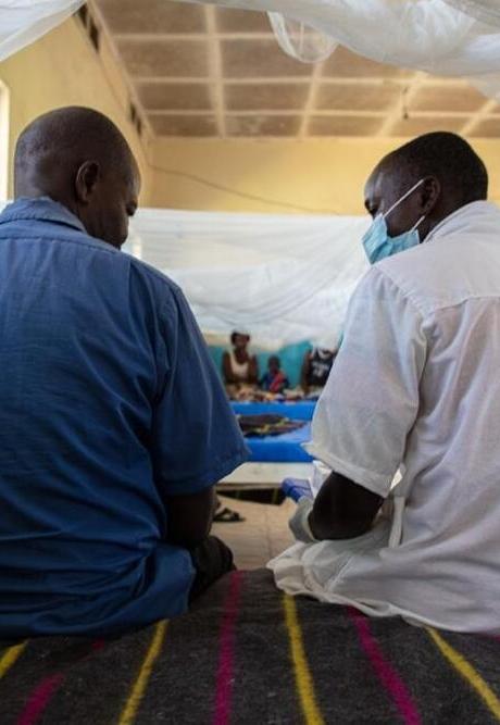 A doctor and a patient sit on a bed as the patient, who had meningitis, is going to be discharged