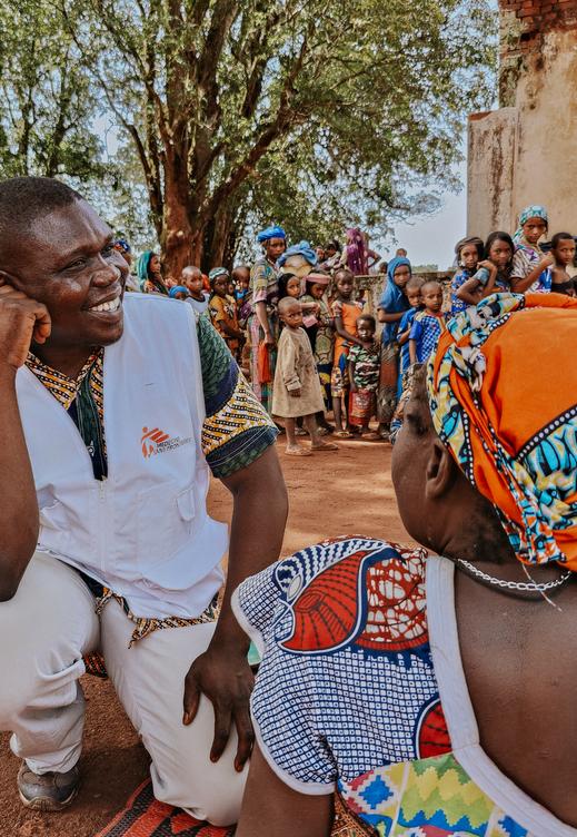A doctor administers a meningitis vaccination to a woman. In the background is a long queue of people waiting for their turn to be vaccinated.