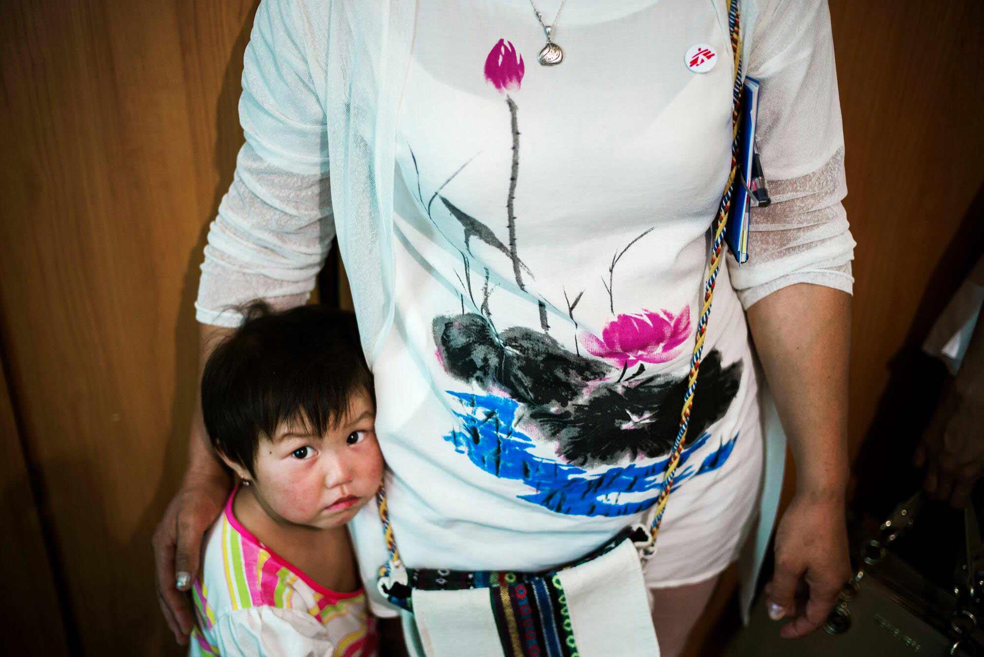 A little girl stands against her mother, who holds her close, at Osh TB paediatric hospital
