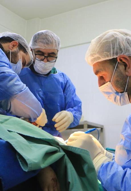 Three doctors in blue scrubs are performing surgery.