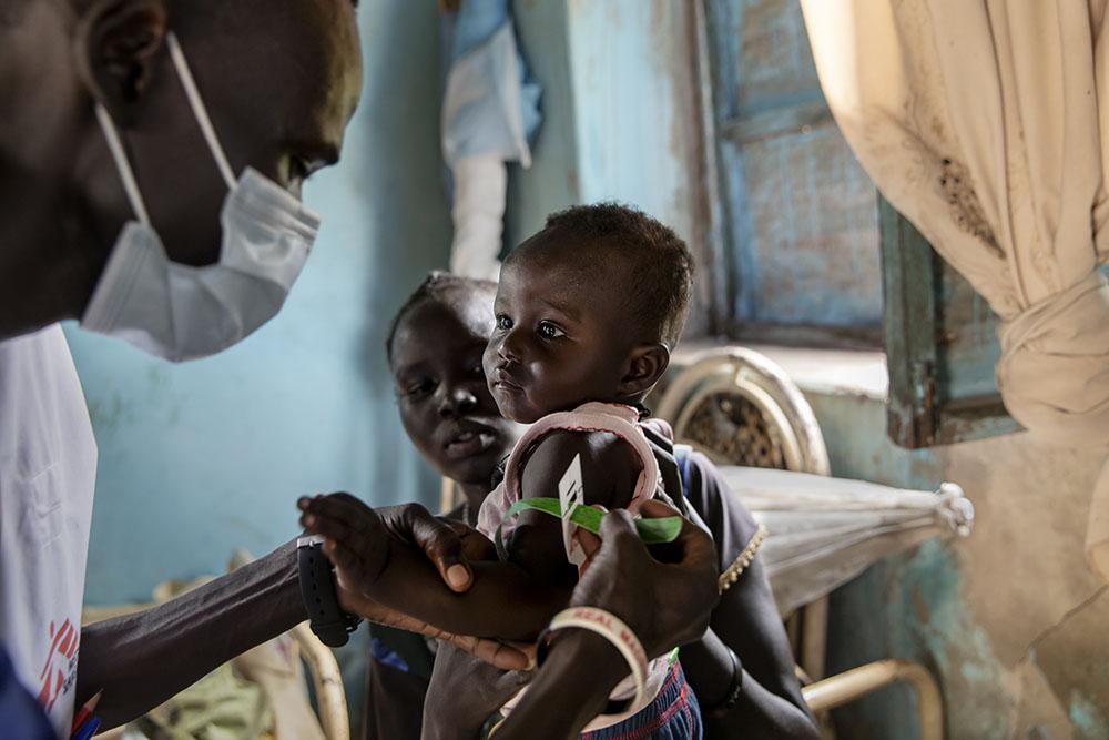 Ajok Atak (age unknown), holds her baby Yel as a member of MSF staff measures the child’s level of nutrition in her house near the village of Kuom, South Sudan, October 26th, 2021. 