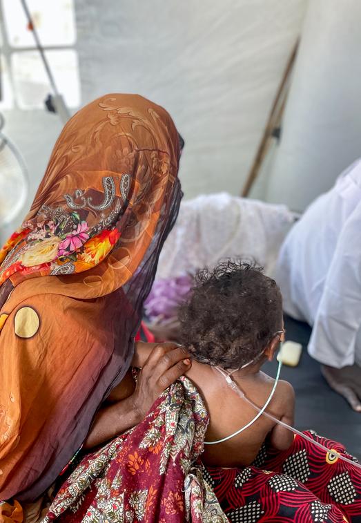 A refugee holds her child inside an MSF medical tent after a Meningitis epidemic broke out in Sudan. 