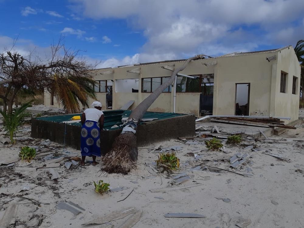 Woman fetching water at a water reservoir in front of a damaged school on Matemo Island