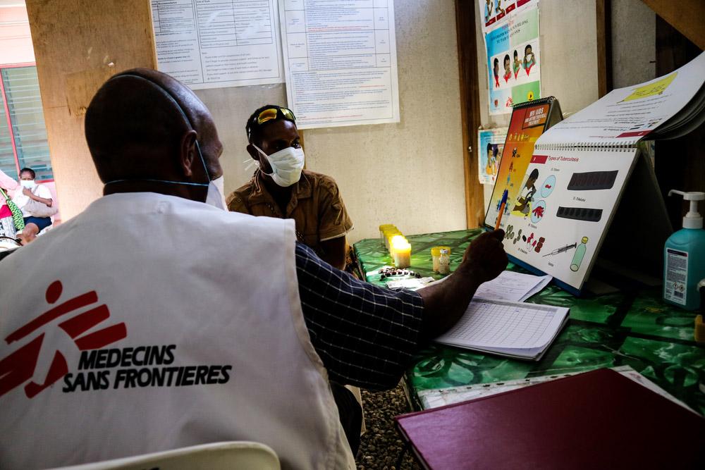 A picture of an MSF healthworker showing a patient TB symptom chart in Papua New Guinea