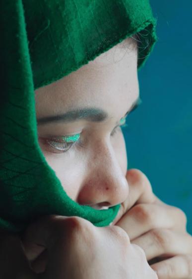 One of our biggest concerns around women's health: sexual and gender-based violence. This is prevalent in refugee camps. Here we see a young victim. She is closing her eyes and a headscarf covers her head. Her hands are over her mouth.