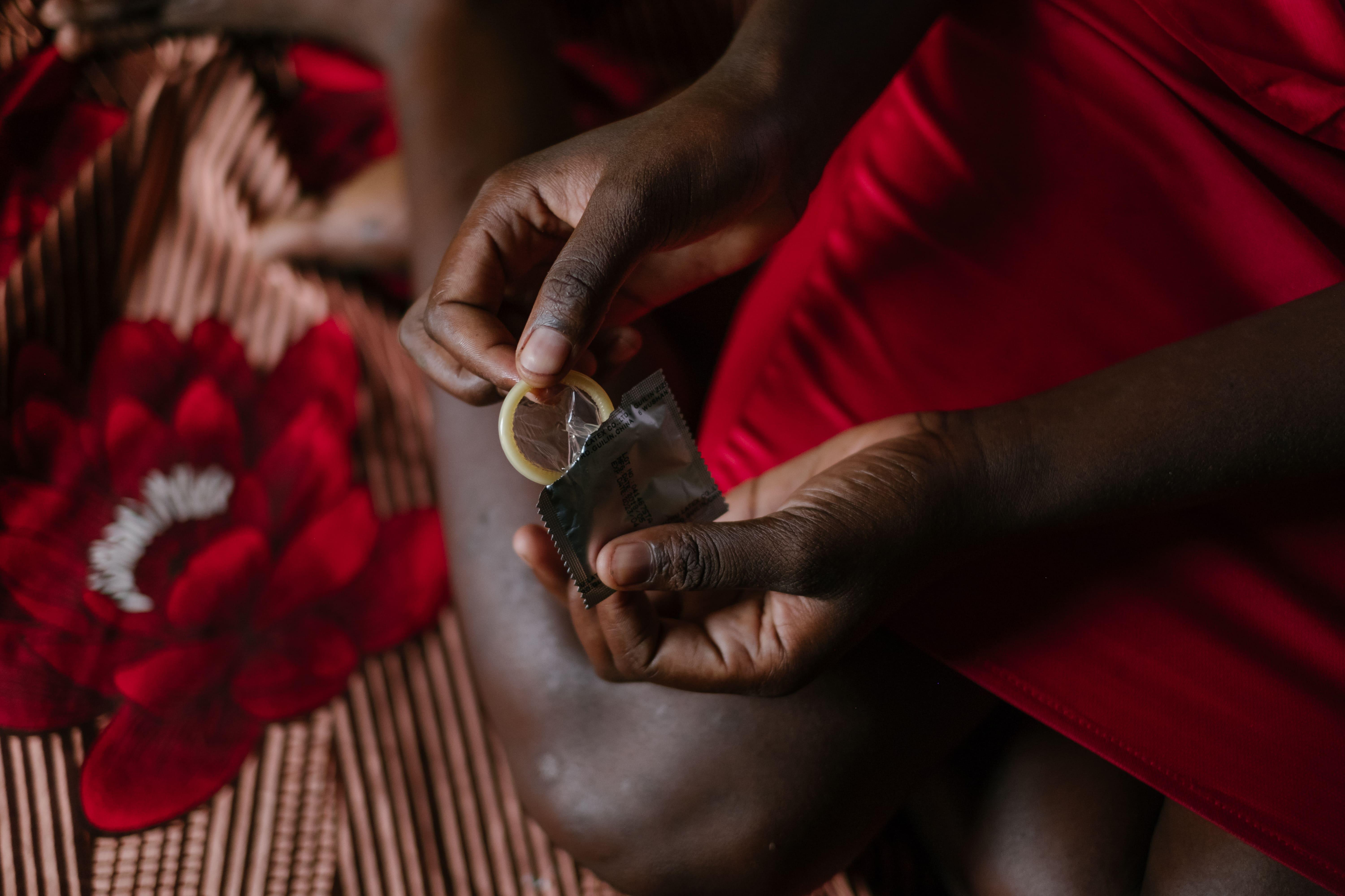 A picture of a sex worker sitting on a on grass mat in a rented room holding a unused condom