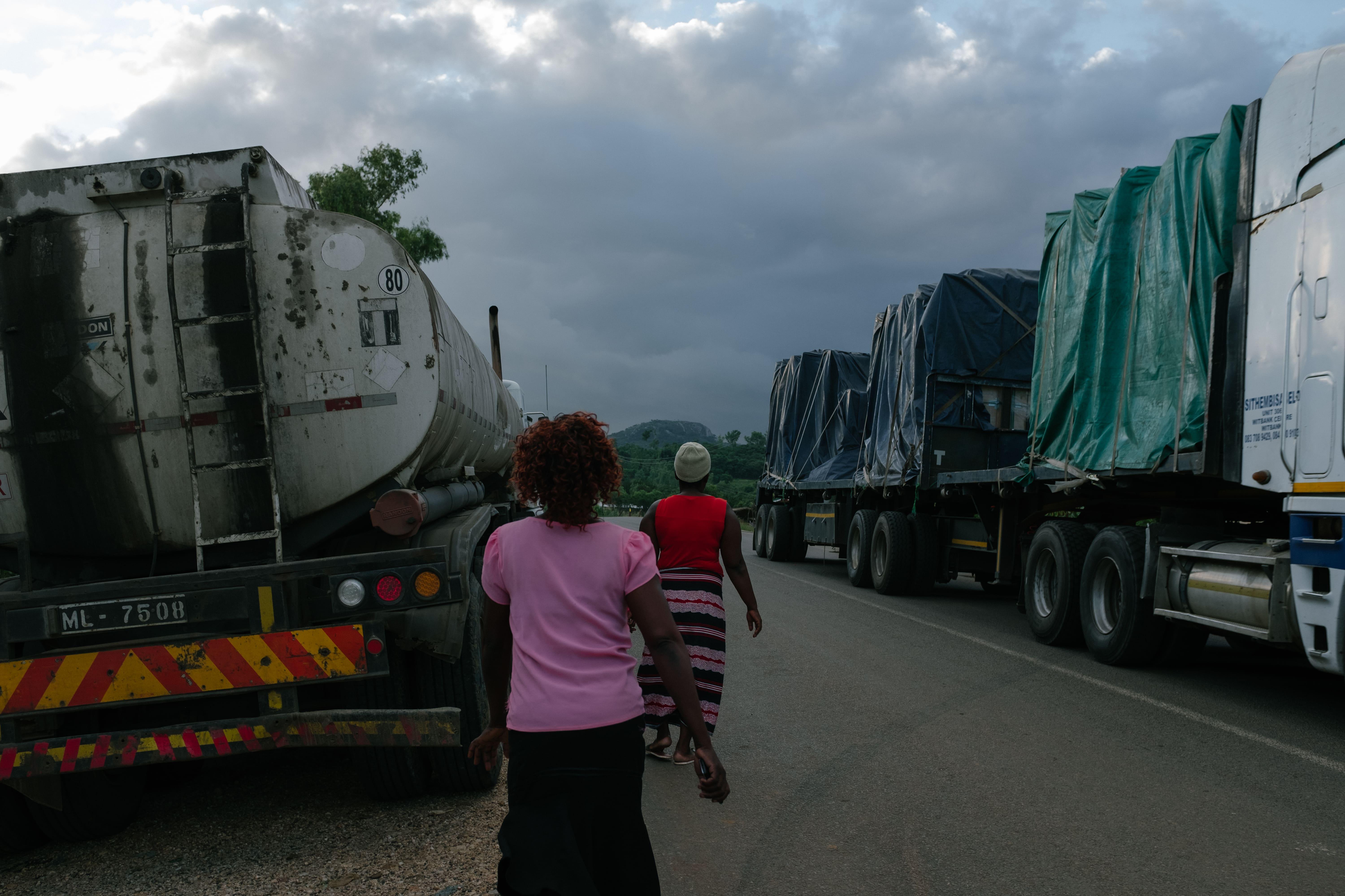 Two MSF communit health workers walking past trucks at Mwanza border post