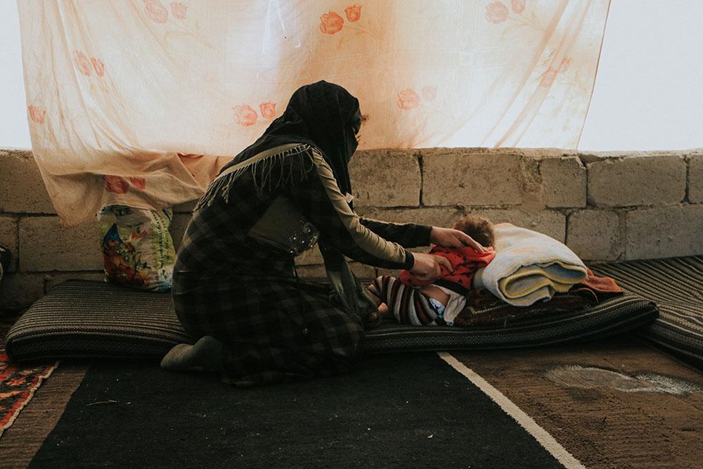 A displaced woman taking care of her daughter inside her tent in a camp in northwest Syria.