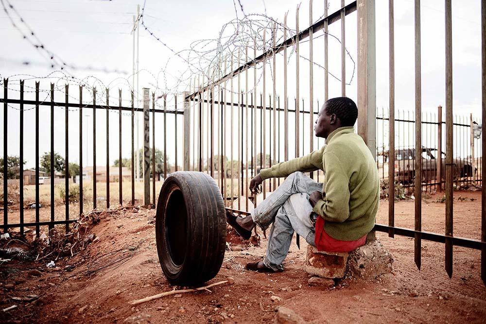 A man is seen looking through the fence line at a temporary shelter where migrants entering South Africa through Musina take refuge.