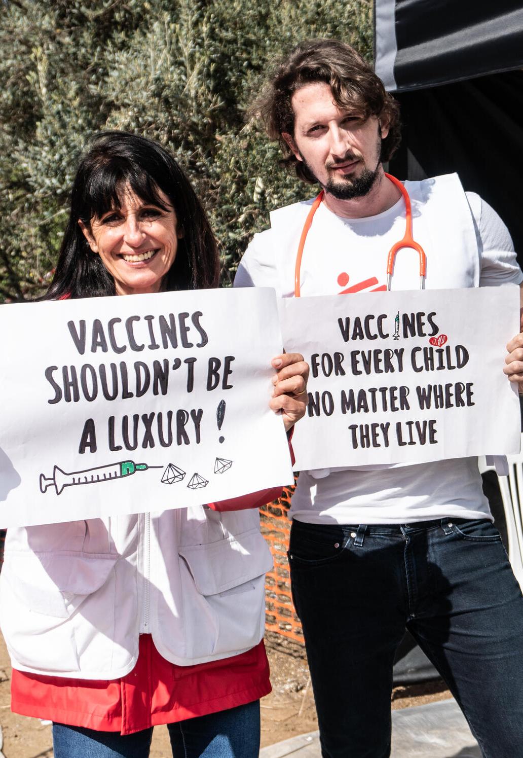 Two staff members hold signs calling for access to medicines